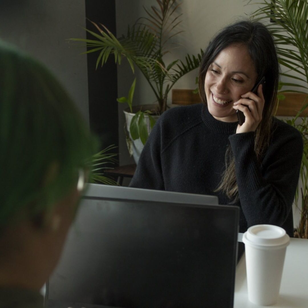 Woman talking on a mobile phone sitting in front of a laptop